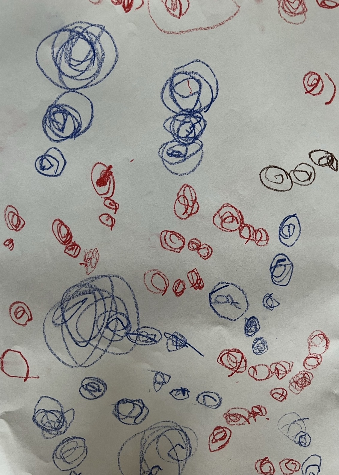 Blue and red circular patterns scattered across paper showing controlled shape-making and color exploration in early childhood drawing