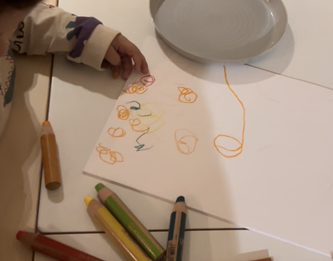 Child drawing with orange crayons showing repeated circular shapes and early symbolic representation typical of ages 2-3