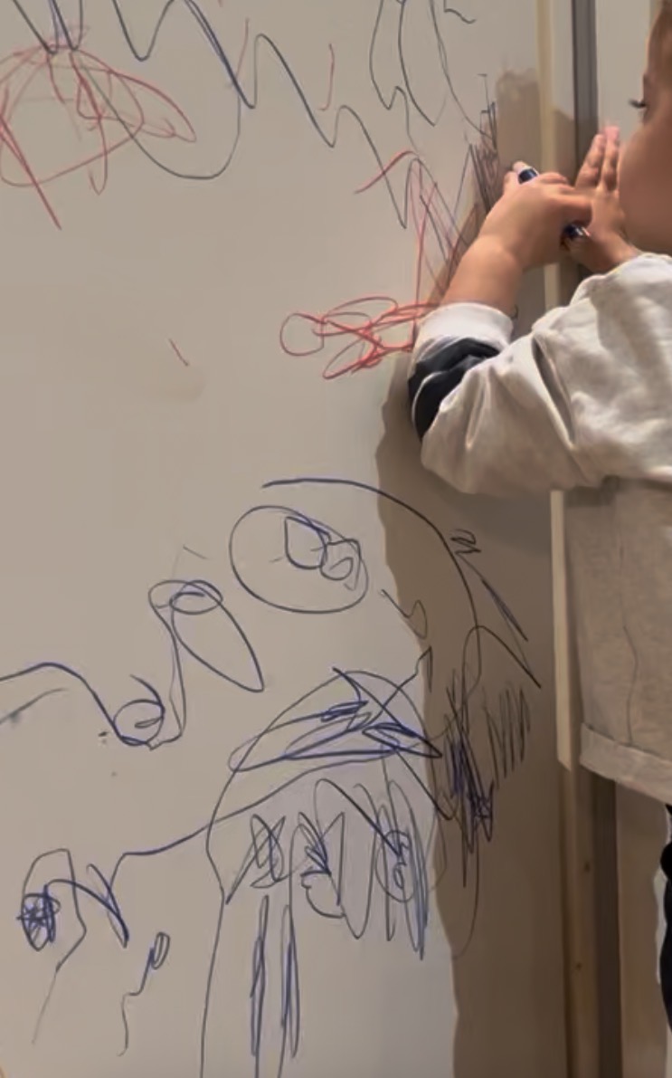 Child drawing on wall showing controlled scribbles evolving into recognizable circular shapes marking transition from random to intentional marks