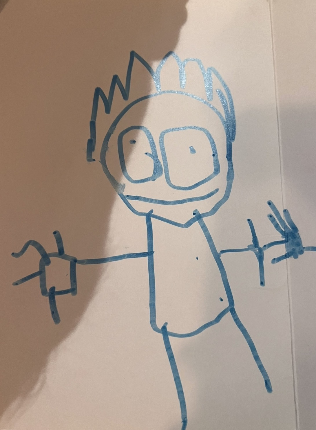 Blue marker drawing of stick figure with torso body fingers and spiky hair showing developmental progression from tadpole to full figure