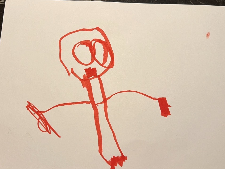 Red marker tadpole person drawing showing classic preschool style with big round head, eyes, smile, and legs coming directly from head