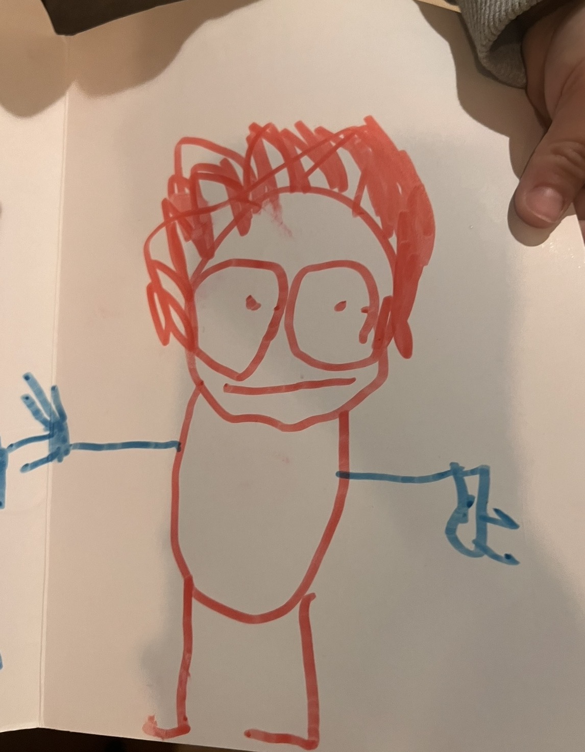 Child drawing of stick figure person with red hair curly details and blue hands showing increasing attention to features and characteristics