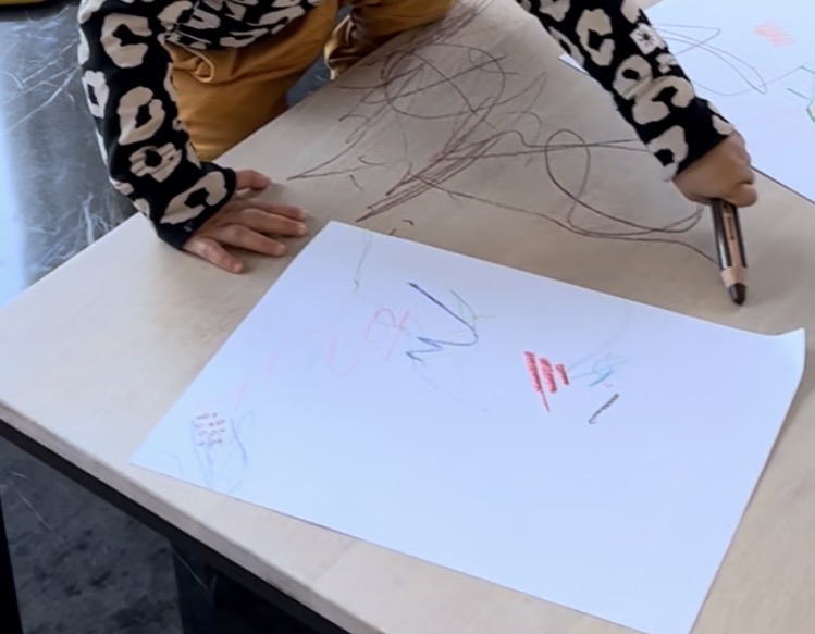 Toddler at table creating colorful crayon scribbles showing random marks and movement exploration typical of ages 1-2